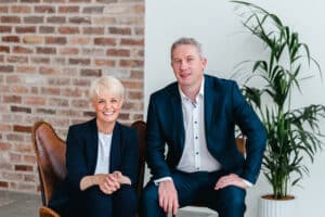 Sarah & Niall Reck from Graphedia, in navy suits sitting in office.